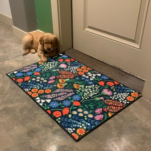 May include: A black and white floral patterned doormat with a golden retriever puppy lying on the floor next to it.