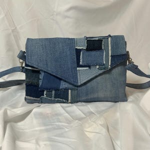 May include: A denim patchwork crossbody bag with a flap closure. The bag features a variety of blue denim patches, creating a textured and unique design. It has a long, adjustable strap and metal hardware.