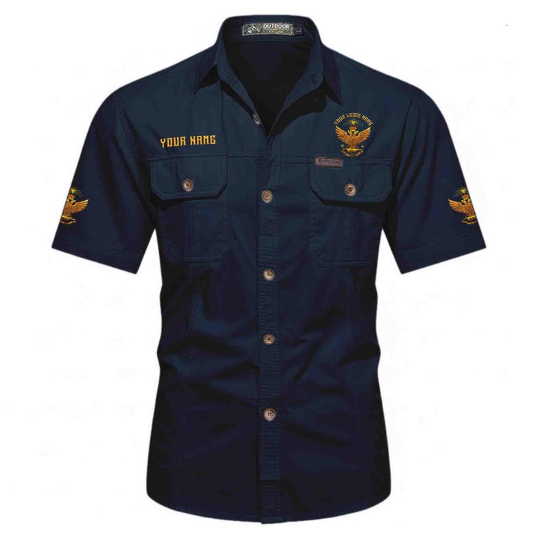 Puede incluir: Camisa azul marino de manga corta con dos bolsillos en el pecho y botones. Presenta dise&ntilde;os de &aacute;guilas bordadas en dorado en las mangas y el pecho. El texto "YOUR NAME" est&aacute; sobre el bolsillo izquierdo y "YOUR LEGEND HERE" sobre el derecho.