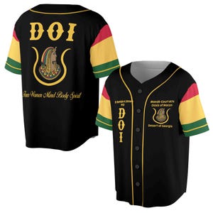 Könnte beinhalten: Schwarzes Baseballtrikot mit goldenen Verzierungen und den Buchstaben DOI auf der Vorderseite. Das Trikot hat einen gelben, roten und grünen Streifen an den Ärmeln. Die Rückseite des Trikots trägt den Text "Five Women Mind Body Spirit" und ein goldenes Emblem mit einem Frauenkopf.