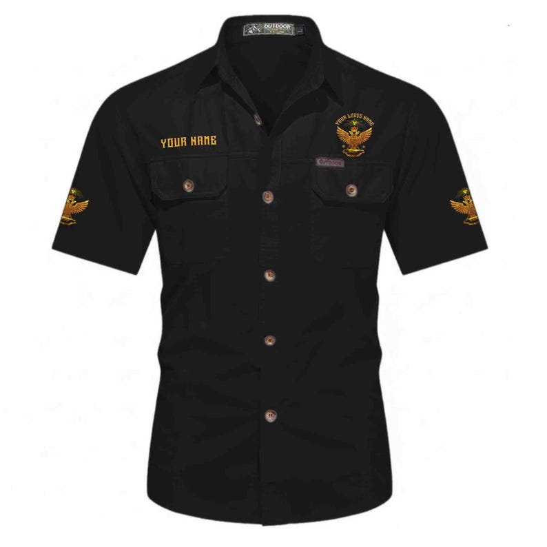 Puede incluir: Camisa negra de manga corta con dos bolsillos en el pecho y cierre de botones. La camisa presenta texto dorado que dice "YOUR NAME" y "YOUR LEADER NAME" junto con emblemas de &aacute;guila dorados. La camisa est&aacute; etiquetada como "OUTDOOR" en la parte superior.