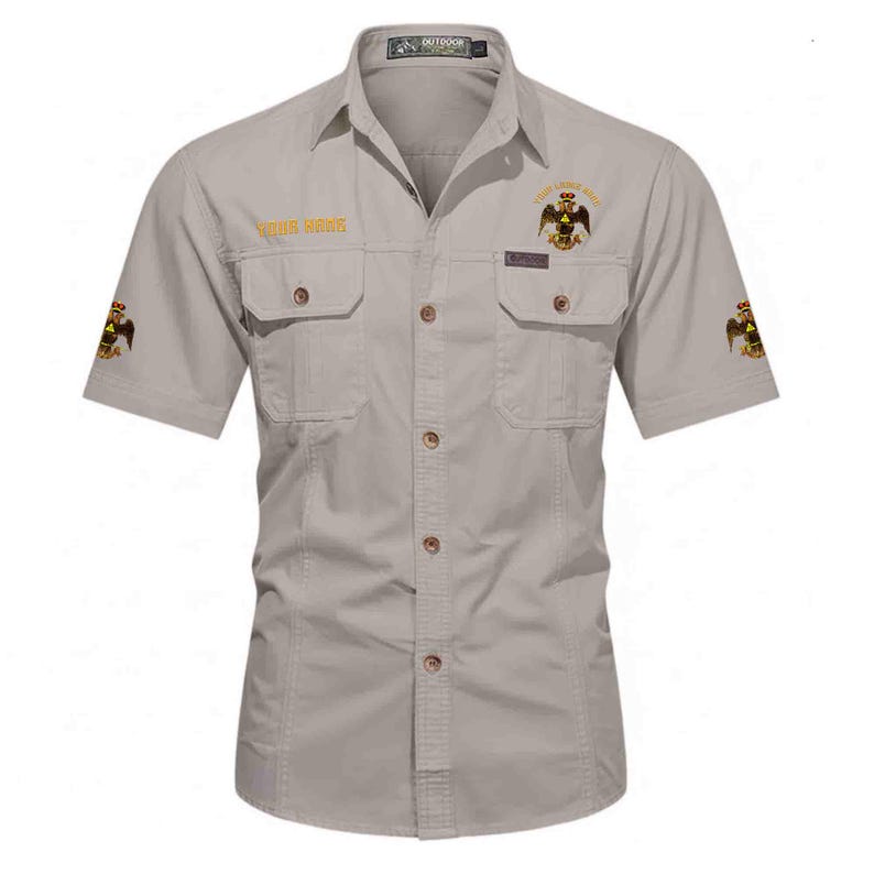 Puede incluir: Una camisa de manga corta abotonada en color beige claro con dos bolsillos en el pecho con solapa. La camisa presenta emblemas bordados de &aacute;guilas bic&eacute;falas doradas en el pecho y las mangas, con el texto "YOUR NAME" en dorado en el pecho derecho.