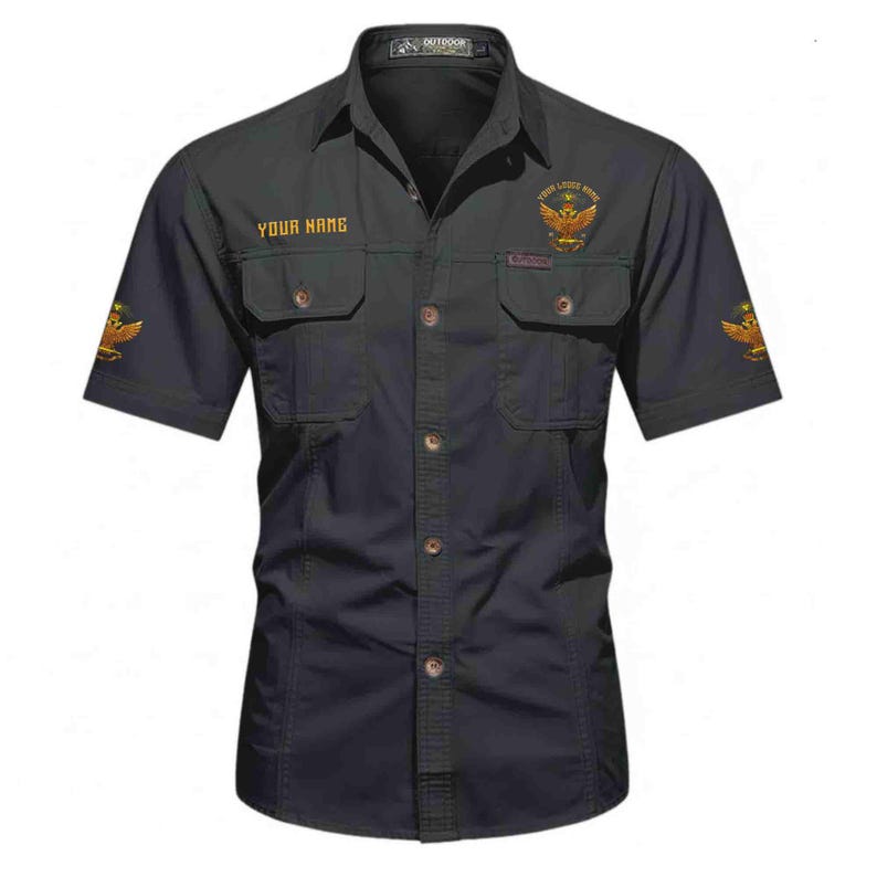 Puede incluir: Camisa negra de manga corta con dos bolsillos en el pecho y botones. La camisa presenta emblemas de &aacute;guila dorados en las mangas y el pecho, con el texto "YOUR NAME" y "YOUR LIFE MATTERS" en dorado.