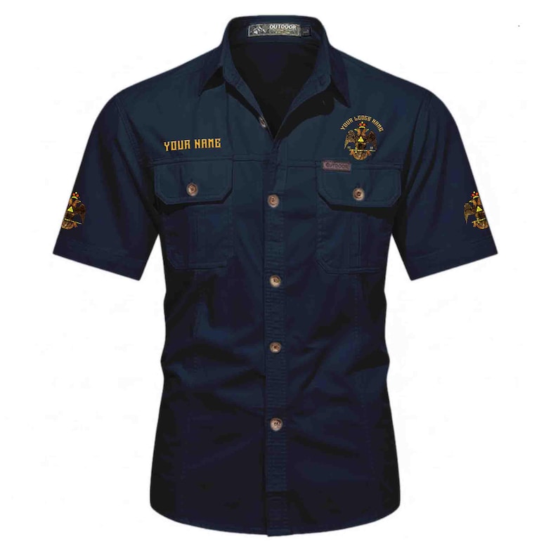 Puede incluir: Una camisa azul marino oscuro de manga corta con botones, dos bolsillos en el pecho, cuello y bordados dorados. El texto "YOUR NAME" est&aacute; impreso en el pecho derecho, mientras que un emblema de &aacute;guila bic&eacute;fala aparece en el pecho izquierdo y las mangas.