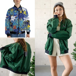 May include: Two green bomber jackets with a black zipper and black ribbed cuffs. One jacket has a colorful graphic print with the text "Cool" and "Survive". The other jacket has a small "m" logo on the right side.