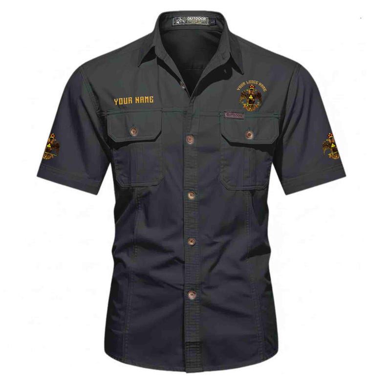 Puede incluir: Una camisa de manga corta gris oscuro con dos bolsillos en el pecho con solapas, cuello y tapeta de botones central. La camisa muestra el texto YOUR NAME y un emblema dorado de &aacute;guila bic&eacute;fala en el pecho y en ambas mangas.