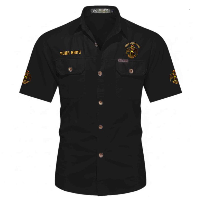 Puede incluir: Una camisa negra de manga corta con botones y dos bolsillos en el pecho con solapa. La camisa muestra el texto "YOUR NAME" en el pecho derecho y un emblema de &aacute;guila bic&eacute;fala dorada en el pecho izquierdo y en ambas mangas.