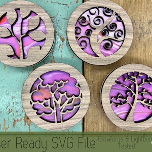 May include: Four wooden coasters with laser cut designs of trees. The coasters are made of wood with a purple and pink marbled finish. The designs are intricate and detailed. The coasters are perfect for adding a touch of nature to your home decor.