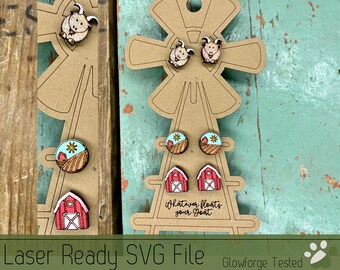 May include: Laser cut wooden earrings featuring a red barn, a field of wheat, and a sun, and a goat. The earrings are displayed on a brown wooden windmill with the text "Whatever floats your goat".