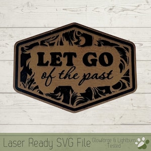 Op de afbeelding: Een bruin zeshoekig bord met een zwarte sierlijke rand en de tekst "LET GO of the past" in zwarte letters.