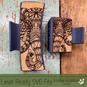 Puede incluir: Dos pinzas para el pelo con base azul oscuro y parte superior de corcho. La parte superior de corcho tiene un diseño de elefante grabado con láser con patrones intrincados. El texto "Glowforge & Lightburn Tested" es visible en la imagen.