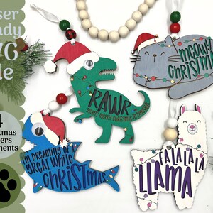 May include: Four laser-cut wooden Christmas ornaments featuring a dinosaur, a cat, a shark, and a llama. Each ornament has a festive Christmas theme and includes text such as "RAWR means Merry Christmas in Dino-saur", "Meow Christmas", "I'm dreaming of a Great White Christmas", and "Fa La La La Llama".