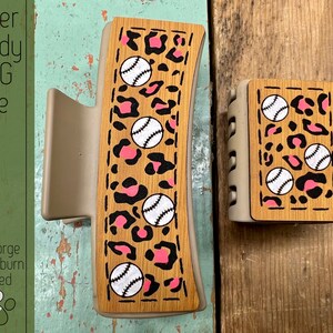 May include: Two wooden hair clips with a pink and black leopard print and white baseballs. The clips are laser cut and ready to be used.