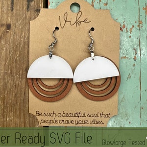 May include: A pair of laser-cut wooden earrings with a white top half and three brown rings. The earrings are hanging from silver hooks. The text "Vibe" is written on a brown card behind the earrings. The text "Be such a beautiful soul that people crave your vibes." is written below the earrings. The text "Laser Ready SVG File Glowforge Tested" is written at the bottom of the image.