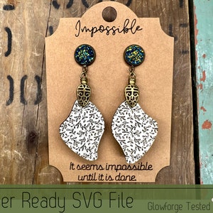 May include: A pair of earrings with a white and black floral design, gold accents, and teal and green glitter embellishments. The earrings are displayed on a brown card with the text "Impossible. It seems impossible until it is done." and "Laser Ready SVG File. Glowforge Tested."