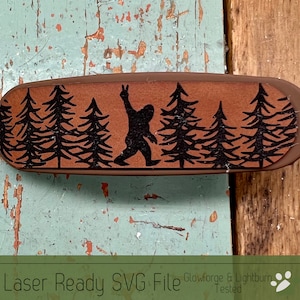 May include: A brown leather hair clip with a black silhouette of a Bigfoot walking through a forest of pine trees. The text "Laser Ready SVG File Glowforge & Lightburn Tested" is printed below the image.