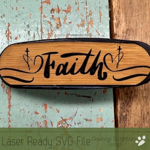 May include: A laser-cut wooden sign with a black border, featuring the word "Faith" in a cursive font with a heart and cross design on either side. The sign is on a rustic wooden background.