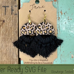 May include: A pair of leopard print wood earrings with black tassel fringe. The earrings are hanging on a brown card with the text "You are a leopard pretending to be a housecat." and "Laser Ready SVG File GlowForge Tested".