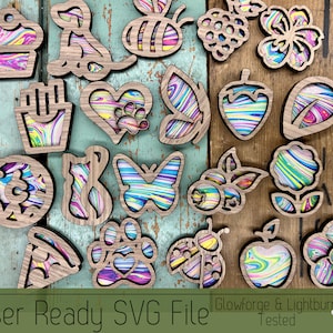 Puede incluir: Un conjunto de 18 adornos de madera cortados con láser con diseños de mármol coloridos. Los adornos presentan varias formas, incluyendo una magdalena, un perro, una abeja, una flor, un corazón, una mariposa, una hoja, una dona, un gato, una huella de pata, una mariquita, una manzana y una flor. Los adornos son perfectos para agregar un toque de fantasía a cualquier decoración del hogar.