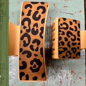 May include: Two hair clips with a leopard print design on a woodgrain background. The clips are a light brown color. The text "Laser Ready SVG File" and "Glowforge & Lightburn Tested" is visible in the image.