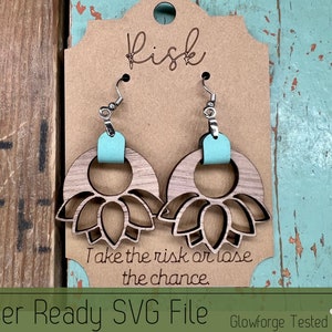 Könnte beinhalten: Ein Paar lasergeschnittene Holzohrringe mit einem floralen Design. Die Ohrringe sind hellblau lackiert und haben silberne Haken. Die Ohrringe werden auf einer braunen Karte mit dem Text "Risk, Take the risk or lose the chance." präsentiert.