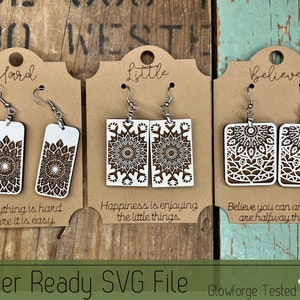 May include: Three pairs of laser-cut wooden earrings with intricate mandala designs. The earrings are displayed on brown cardstock with the words "Hard", "Little", and "Believe" written on them. The text below each pair of earrings reads "Everything is hard before it is easy", "Happiness is enjoying the little things", and "Believe you can and you are halfway there".