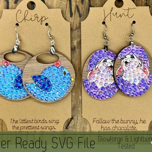 May include: Two pairs of laser-cut wooden earrings. The first pair features a blue bird with rhinestones, and the text "Chirp, The littlest birds sing the prettiest songs." The second pair features a white bunny emerging from an egg with purple rhinestones, and the text "Hunt, Follow the bunny, he has chocolate."