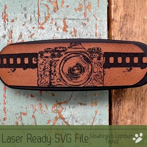 May include: A black and brown wooden camera-shaped keychain with a film strip design. The keychain features a black and white illustration of a vintage camera.