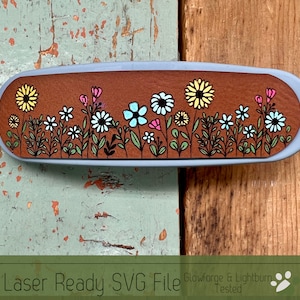 May include: A laser-cut design of a row of colorful flowers on a brown background. The design is ready to be used with a Glowforge or Lightburn laser cutter. The text "Laser Ready SVG File Glowforge & Lightburn Tested" is at the bottom of the image.