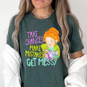 May include: A green t-shirt with a cartoon image of a woman with red hair and a green lizard. The text on the shirt reads "Take Chances Make Mistakes Get Messy".
