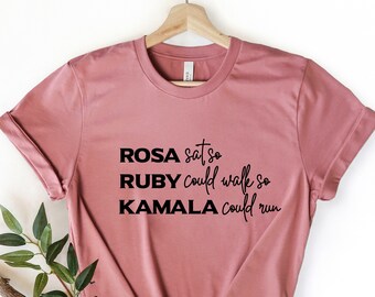 May include: A dusty rose t-shirt with black text that reads "ROSA sat so RUBY could walk so KAMALA could run".
