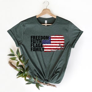 May include: A dark green t-shirt featuring a distressed American flag graphic and the words "Freedom, Faith, Flag & Family" printed in black.