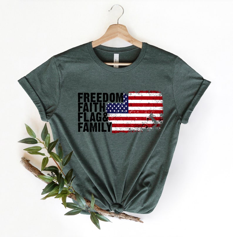 May include: A dark green t-shirt featuring a distressed American flag graphic and the words "Freedom, Faith, Flag & Family" printed in black.