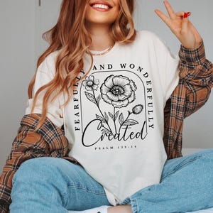 May include: A white long-sleeved shirt with a black floral design and the text "Fearfully and Wonderfully Created Psalm 139:14".