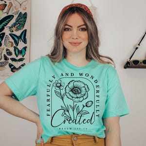 May include: A turquoise t-shirt with a black floral design and the text "Fearfully and Wonderfully Created" with the scripture reference "Psalm 139:14".