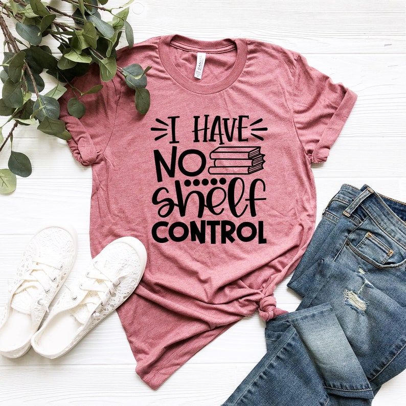 May include: A pink t-shirt with the text "I have no shelf control" in black lettering. The text is accompanied by a graphic of a stack of books.