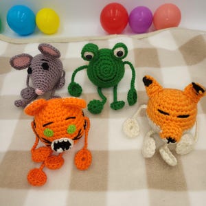May include: A collection of handmade crochet animal toys, including a gray mouse, a green frog, an orange tiger, and an orange fox. The toys are made with yarn and have detailed features. Colorful plastic eggs are in the background.