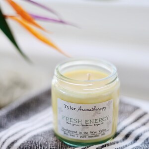 May include: A glass jar candle with a yellow wax and a white label that reads "Tyler Aromatherapy Fresh Energy Black Tea, Mandarin Bergamot Handpoured in the Wye Valley Soy wax + pure essential oils".