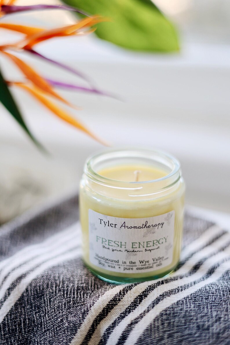 May include: A glass jar candle with a yellow wax and a white label that reads "Tyler Aromatherapy Fresh Energy Black Tea, Mandarin Bergamot Handpoured in the Wye Valley Soy wax + pure essential oils".