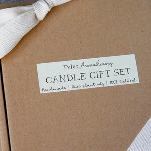 May include: A brown cardboard box with a white ribbon tied around it. The box has a label that says "Tyler Aromatherapy Candle Gift Set Handmade | Pure plant oils | 100% Natural"