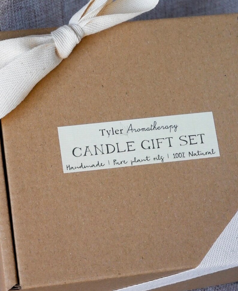May include: A brown cardboard box with a white ribbon tied around it. The box has a label that says "Tyler Aromatherapy Candle Gift Set Handmade | Pure plant oils | 100% Natural"