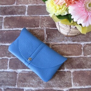 May include: A blue leather clutch purse with a silver button closure. The purse is on a brick background.