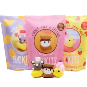 Könnte beinhalten: Drei Pakete mit lufttrocknenden Ton-Sets mit bunten Hintergründen und Illustrationen einer Maus, eines S'mores und einer Schnecke. Der Text auf den Verpackungen lautet "Maisy the Mouse", "S'more Than a Feeling" und "Berry Snailcake".