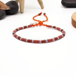 May include: A red and silver beaded bracelet with an orange cord closure.