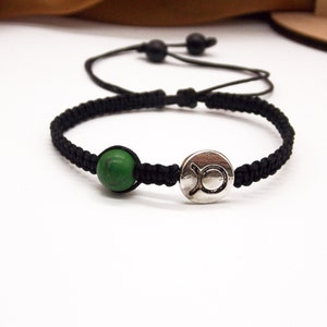 May include: Black braided bracelet with a green bead and a silver charm with the Taurus zodiac symbol.