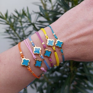 May include: A set of eight colorful bracelets with a gold clover charm. Each bracelet is made of a thin cord and features a turquoise enamel clover charm.