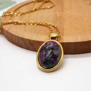 Può includere: Una collana con catena dorata con un ciondolo che presenta una grande pietra preziosa ovale di colore verde e viola incastonata in una cornice dorata.