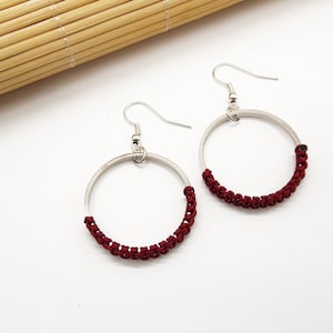 Puede incluir: Un par de pendientes de aro de plata con un cordón burdeos envuelto alrededor de la mitad de cada aro.