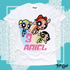 May include: White t-shirt with a graphic of the Powerpuff Girls, the number 3, and the name "ARIEL" in pink letters.