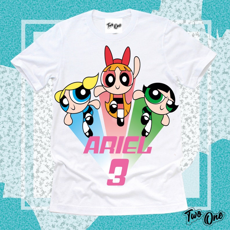May include: White t-shirt with a graphic of the Powerpuff Girls, a pink, blue, and green color scheme, and the text "ARIEL 3".